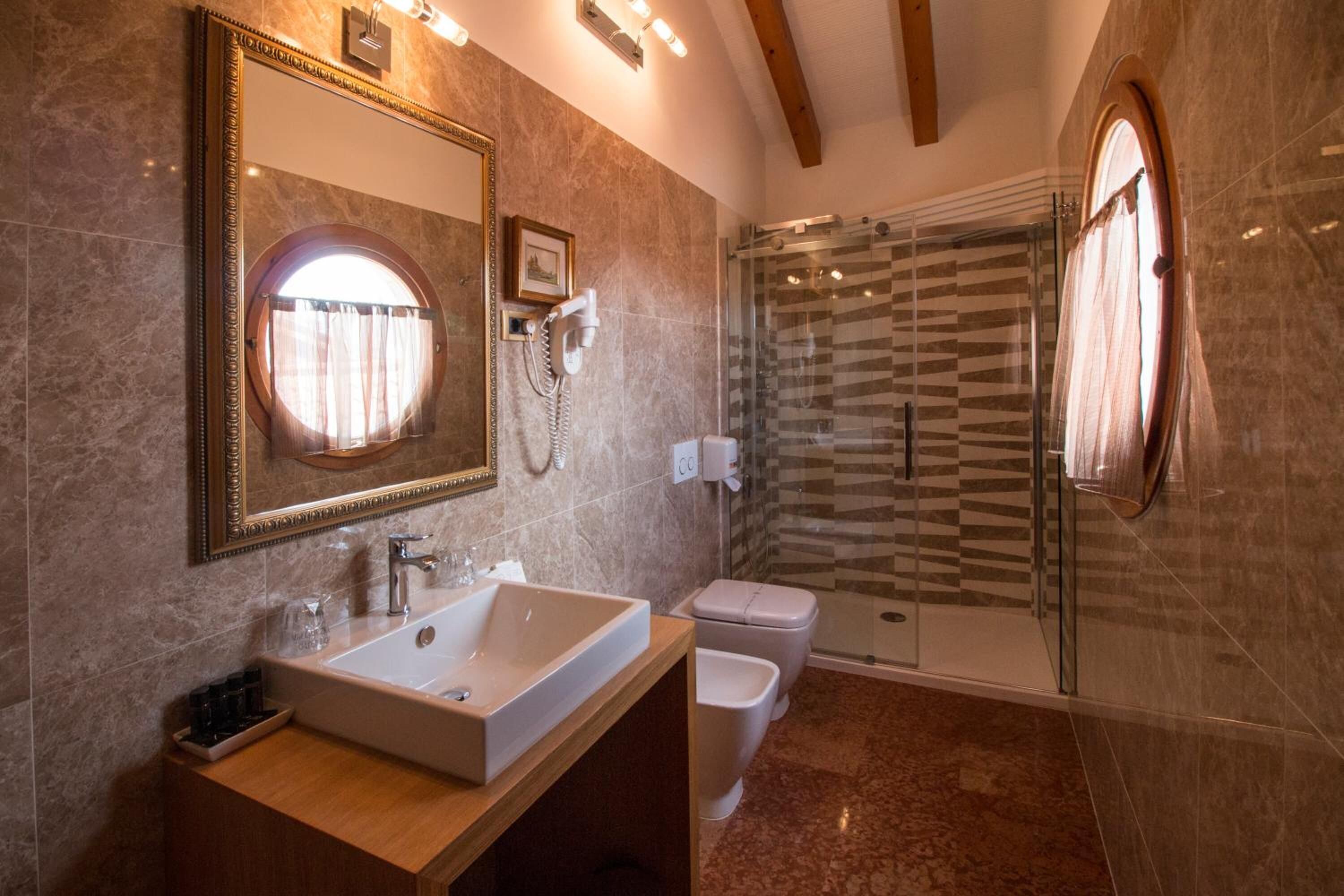 Un baño moderno con un espejo grande, un lavamanos, un inodoro y una ducha con mampara de cristal.