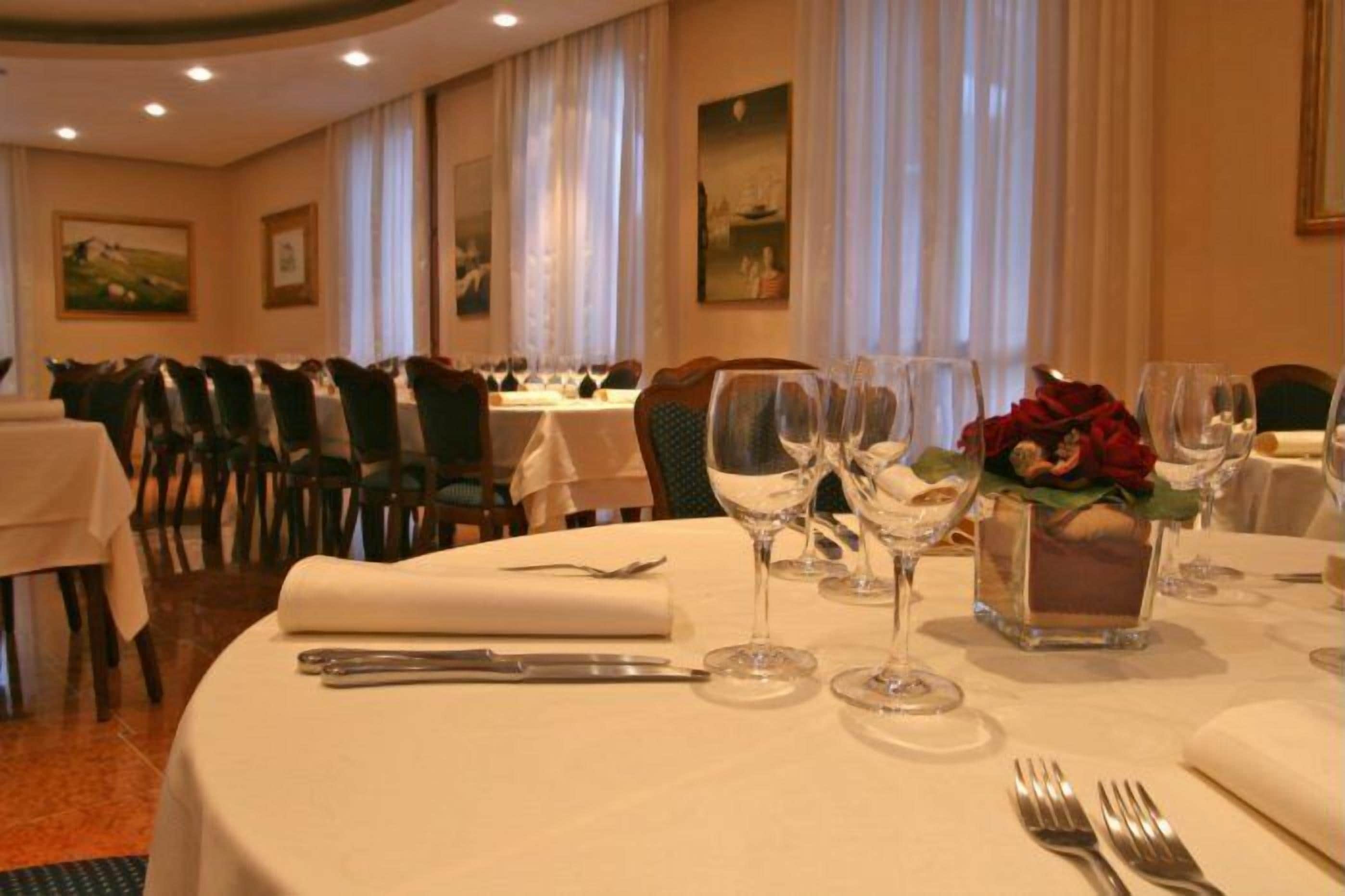 Un comedor con mesas redondas dispuestas para una comida, incluyendo cubiertos y copas de vino.