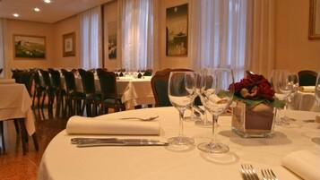 Un comedor con mesas redondas dispuestas para una comida, incluyendo cubiertos y copas de vino.