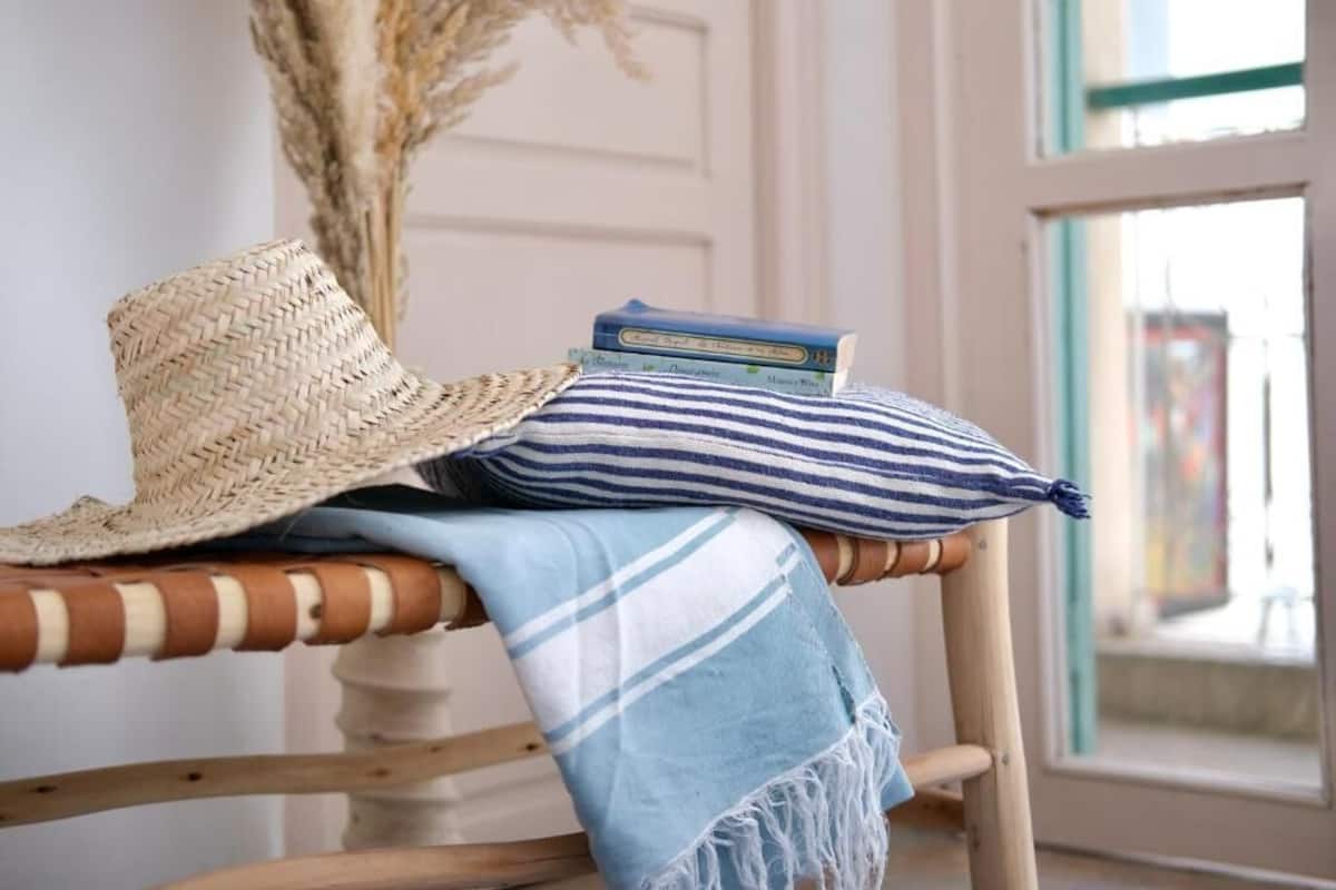 Une chaise en osier surmontée d’un chapeau tressé, un coussin à rayures et une couverture bleue et blanche à rayures.