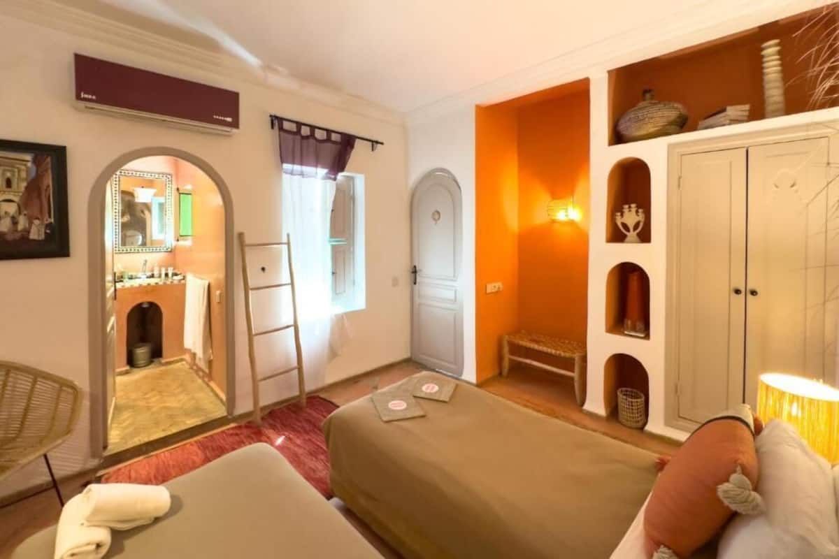 A hotel room with two beds, a bathroom, a kitchenette, and a small seating area.