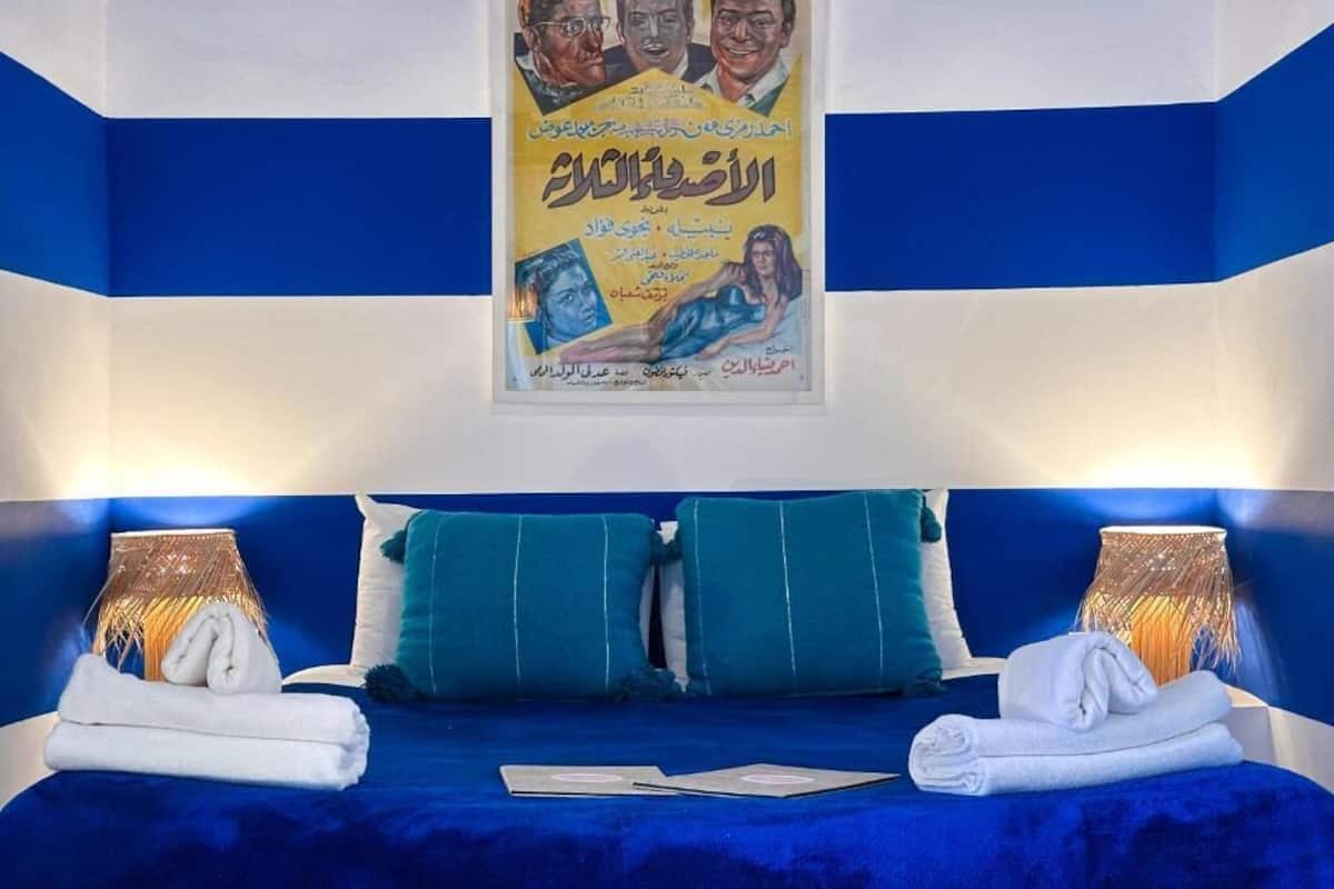 A hotel room with a blue and white color scheme, a bed with teal pillows, two lamps, and a poster on the wall.