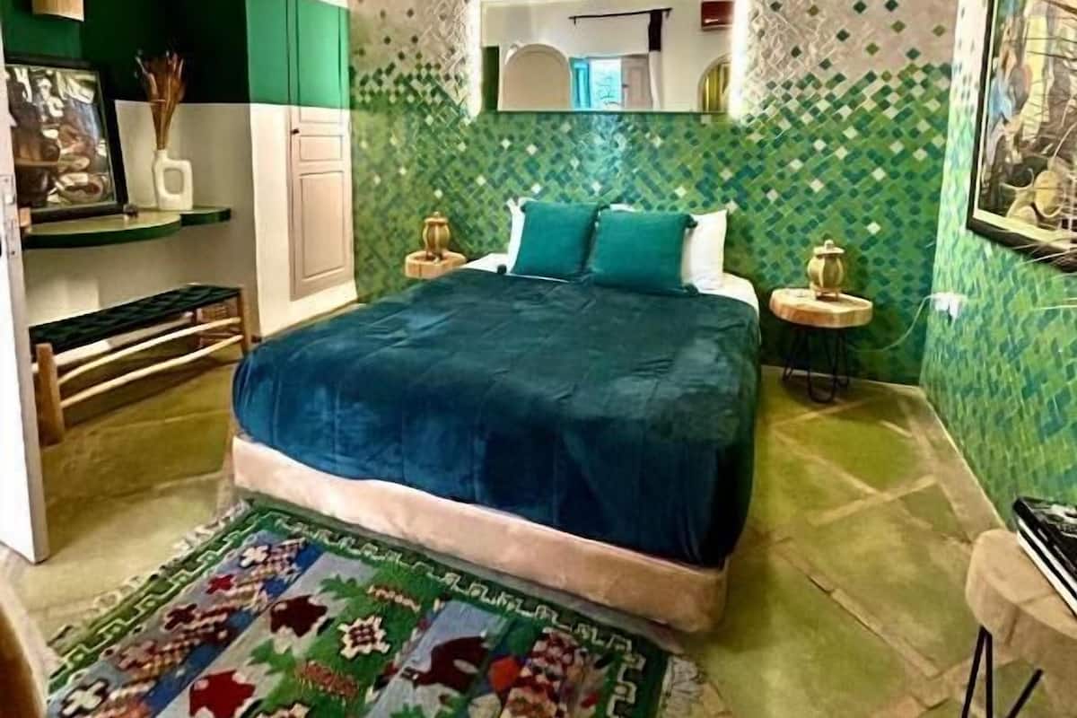 A bedroom with a bed, bedside tables, a mirror, and a patterned rug.