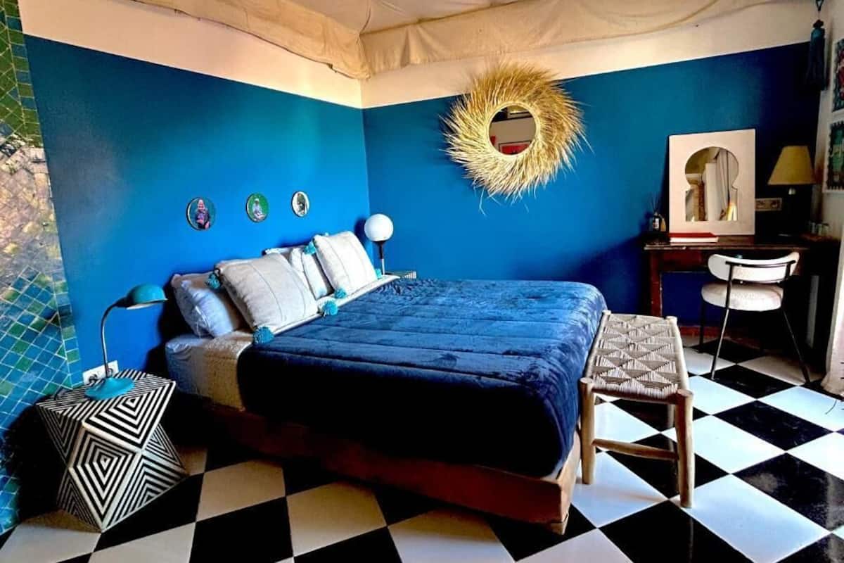 A bedroom with a bed, a chair, a desk, and a mirror.
