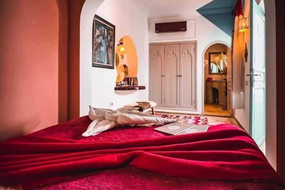A bedroom with a red bedspread, a framed picture on the wall, and a wardrobe.