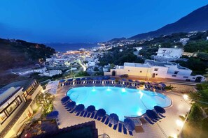 A pool area with lounge chairs and umbrellas, surrounded by buildings with a view of the sea and a mountain in the background. - Albergo Terme San Lorenzo (Forio)