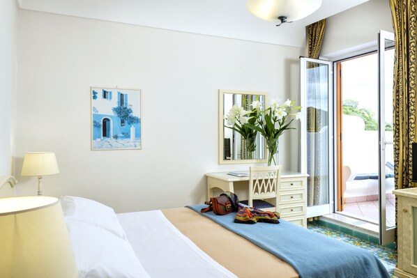Une chambre d’hôtel avec un lit, un bureau, une chaise, une lampe, un vase de fleurs, un tableau et une vue sur l’extérieur.
