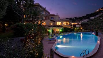 A swimming pool with lounge chairs, surrounded by a landscaped garden and a large building with multiple windows and balconies.