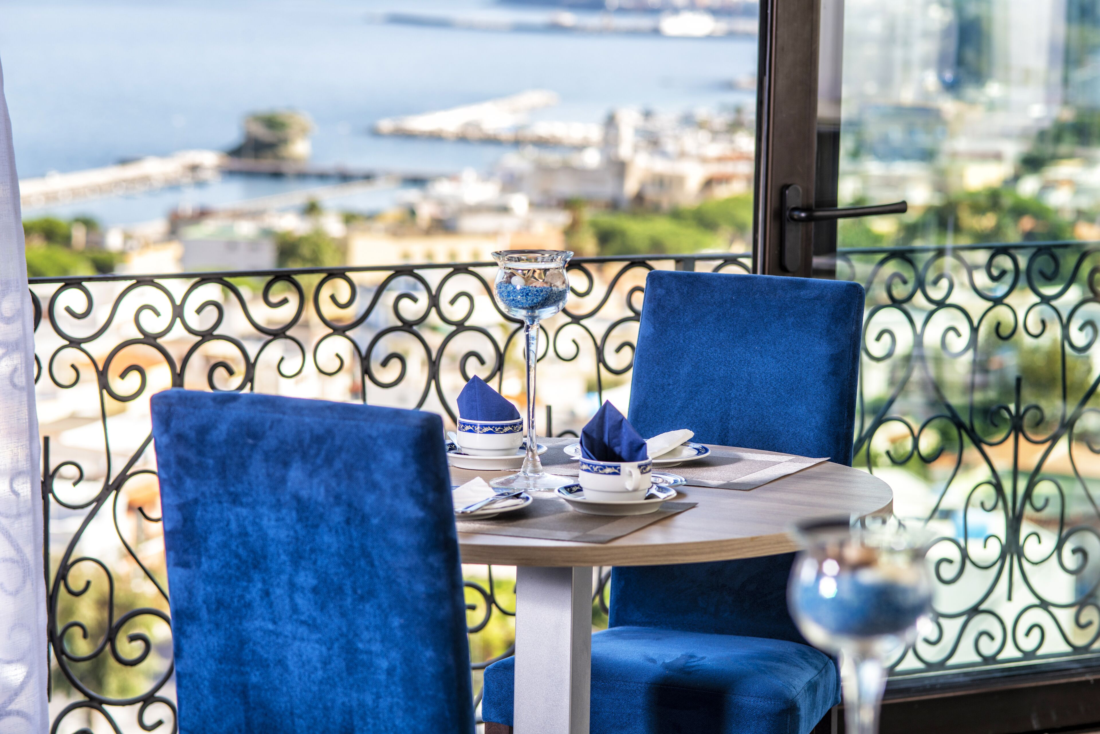 Un tavolo da pranzo con sedie blu, un bicchiere d'acqua e vista su una città e un corso d'acqua.