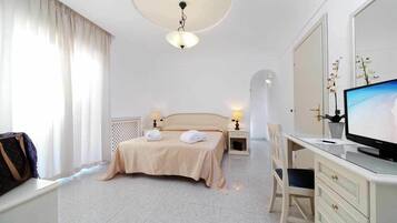 Camera d'albergo con un letto, due lampade ai comodini, una scrivania con un computer, una televisione e una finestra con tende.