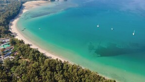 An aerial view of a coastal area with a beach, boats, and a forested hill. - Dewa Phuket Resort & Villas (Sa Khu)