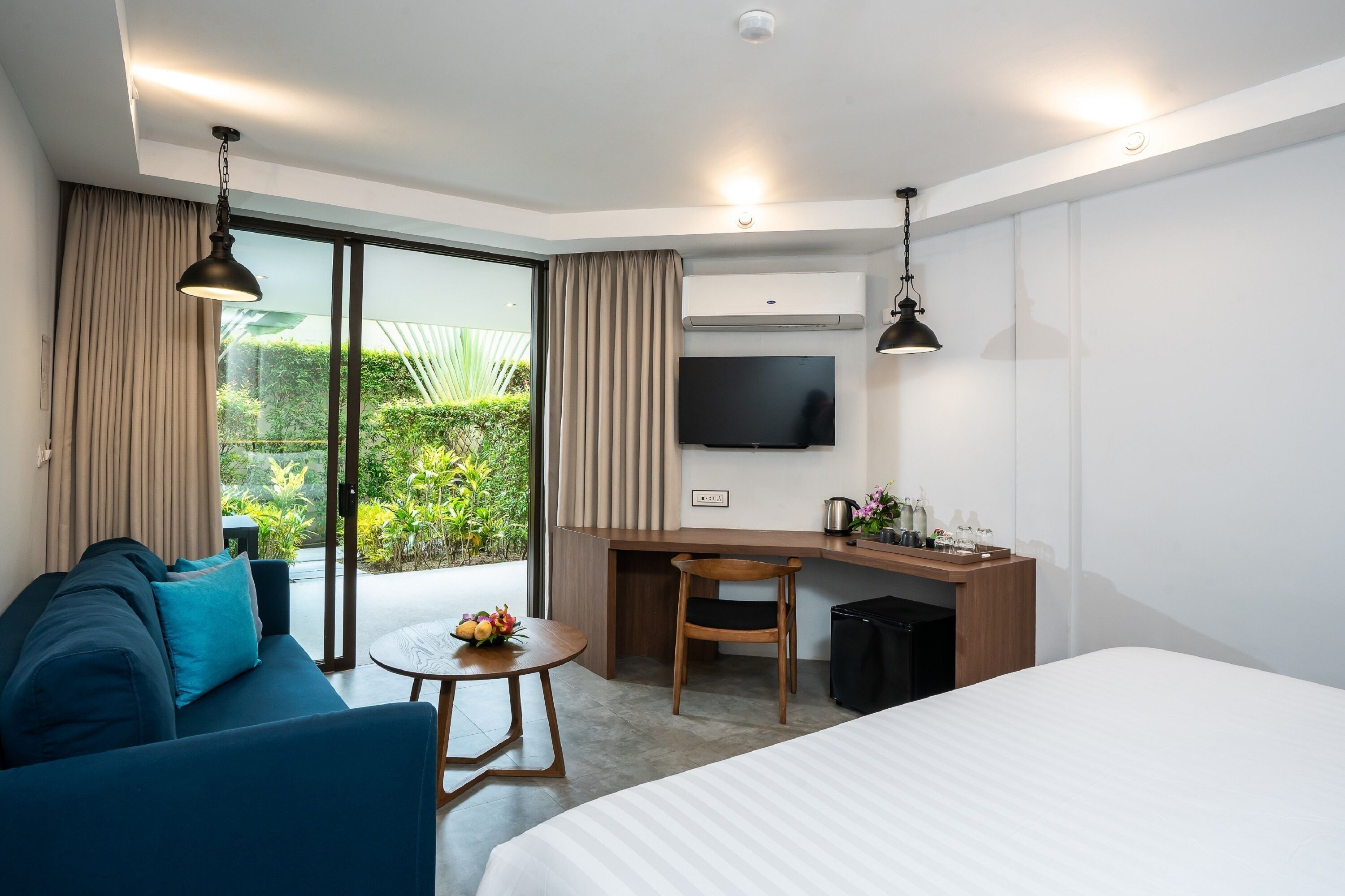 Una habitación de hotel moderna con una cama grande, un sofá, un escritorio con una silla, un televisor y una pequeña mesa con un arreglo floral.