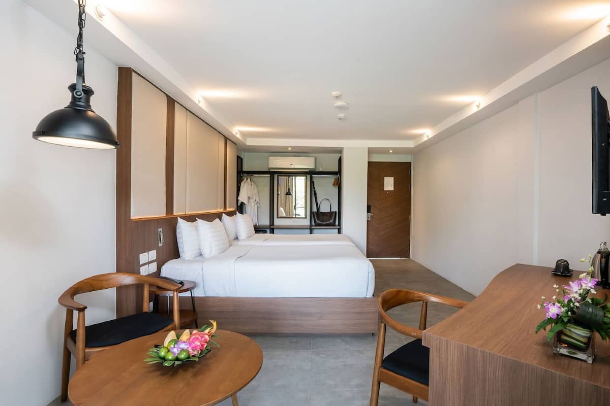 A hotel room with a bed, two wooden chairs, a small round table with a flower arrangement, a TV, and a wardrobe.