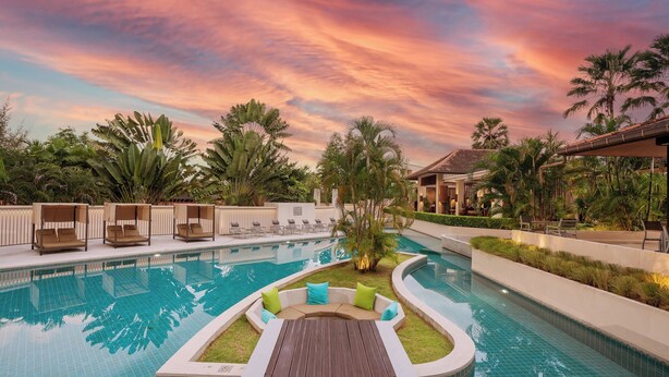 A pool area with a wooden deck and seating, surrounded by palm trees and a sunset sky. - Dewa Phuket Resort & Villas (Sa Khu)