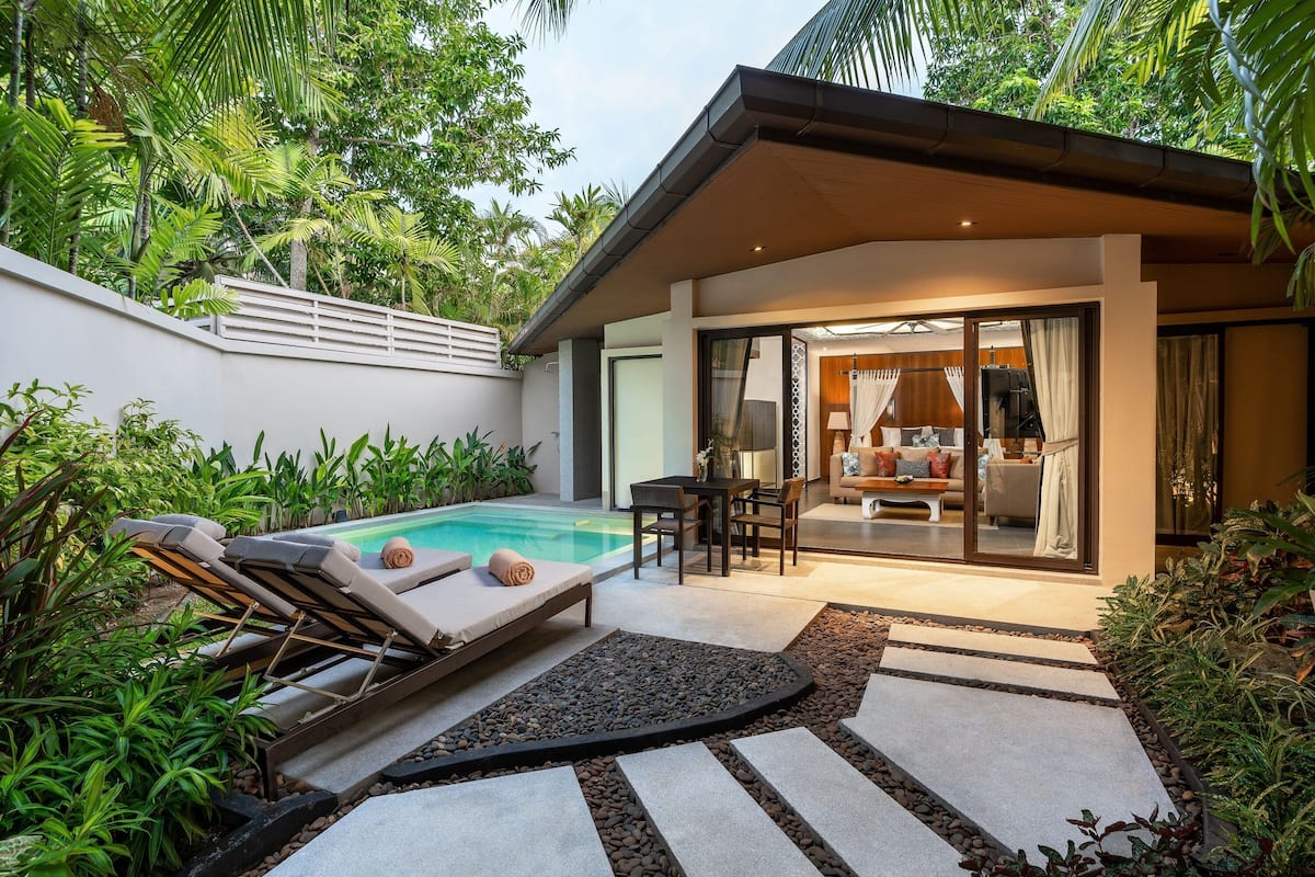 A modern outdoor pool area with lounge chairs, a dining table, and a living area with a sofa and curtains.