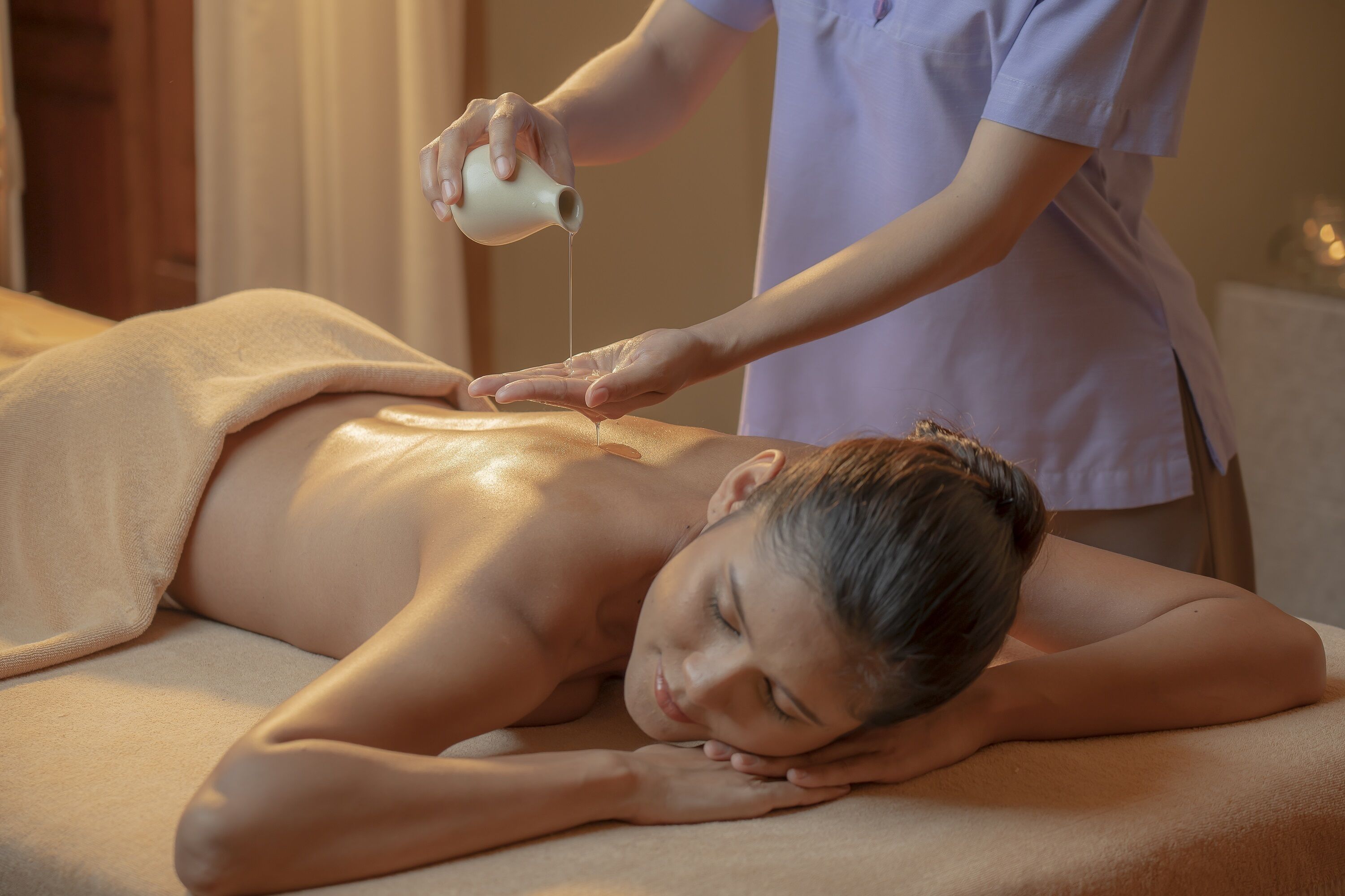 A person receiving a back massage in a room with a massage table and a bottle of oil.