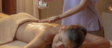 A person receiving a back massage in a room with a massage table and a bottle of oil.