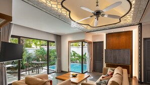 A modern living room with a sofa, coffee table, and TV. There is a pool visible through the glass doors. - Dewa Phuket Resort & Villas (Sa Khu)