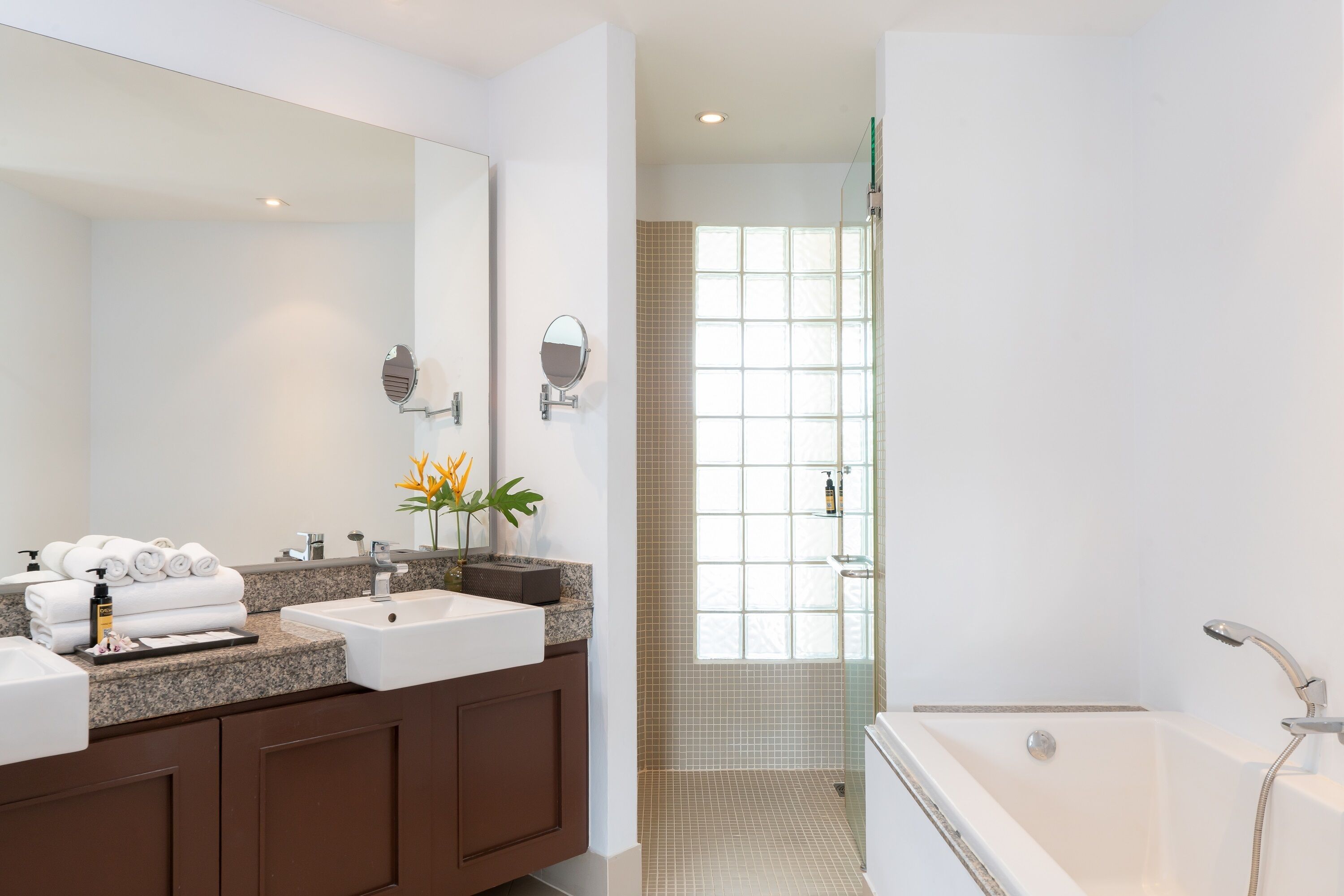 A modern bathroom with a large mirror, two sinks, a bathtub, and a shower area.