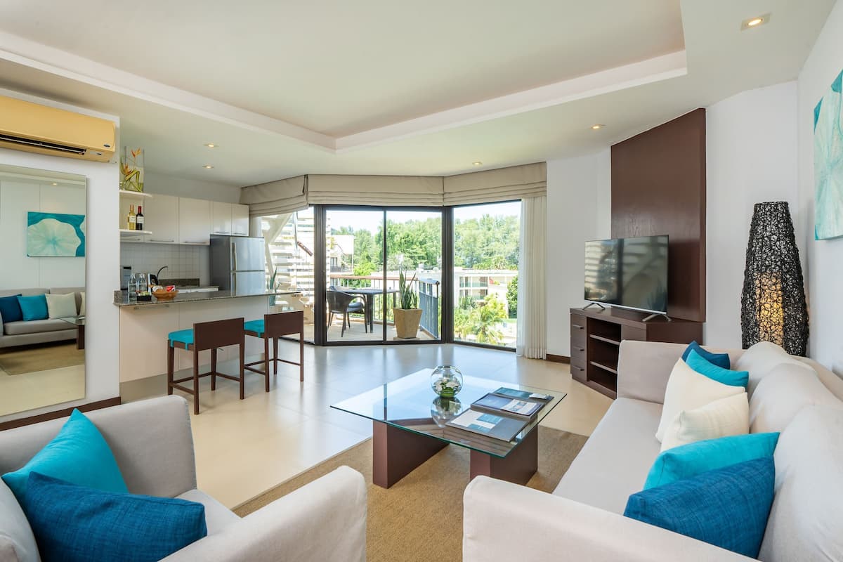 A modern living room with a glass coffee table, a sofa with blue cushions, and a television.