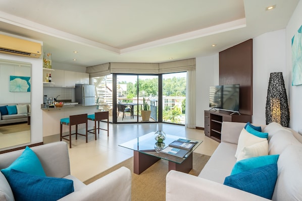 A modern living room with a glass coffee table, a sofa with blue cushions, and a television.