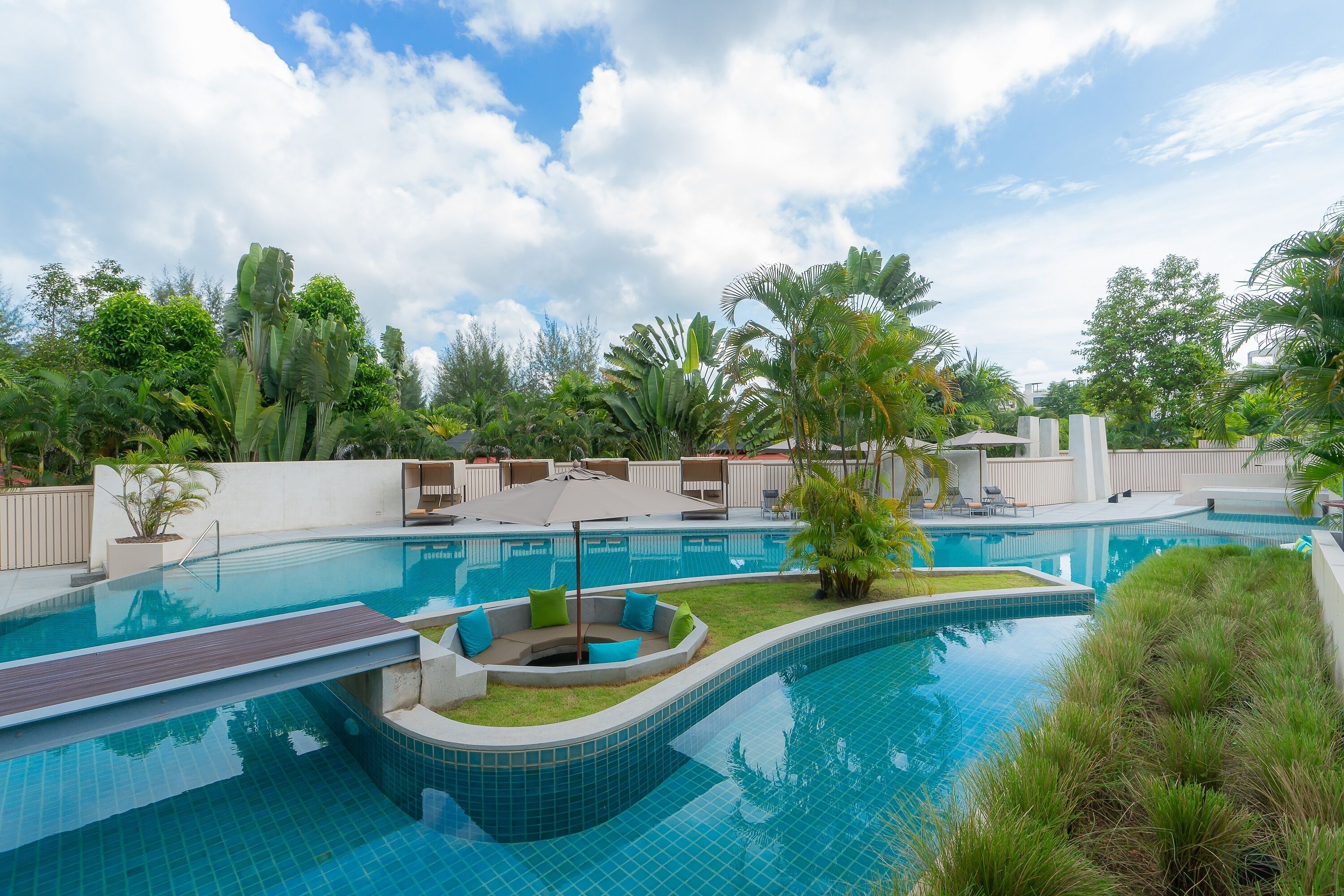 Ein Pool mit gewölbter Kante, umgeben von üppiger Bepflanzung und einem überdachten Sitzbereich mit Stühlen und Sonnenschirmen.