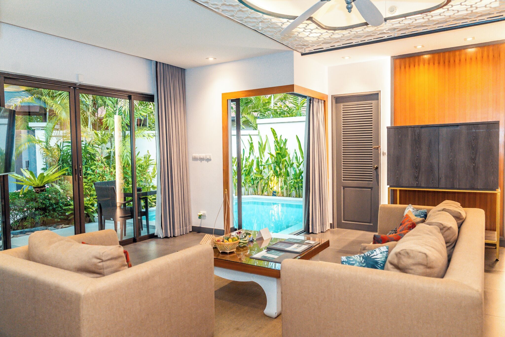 A modern living room with a glass door leading to a pool area, a comfortable sofa set, and a flat-screen TV.