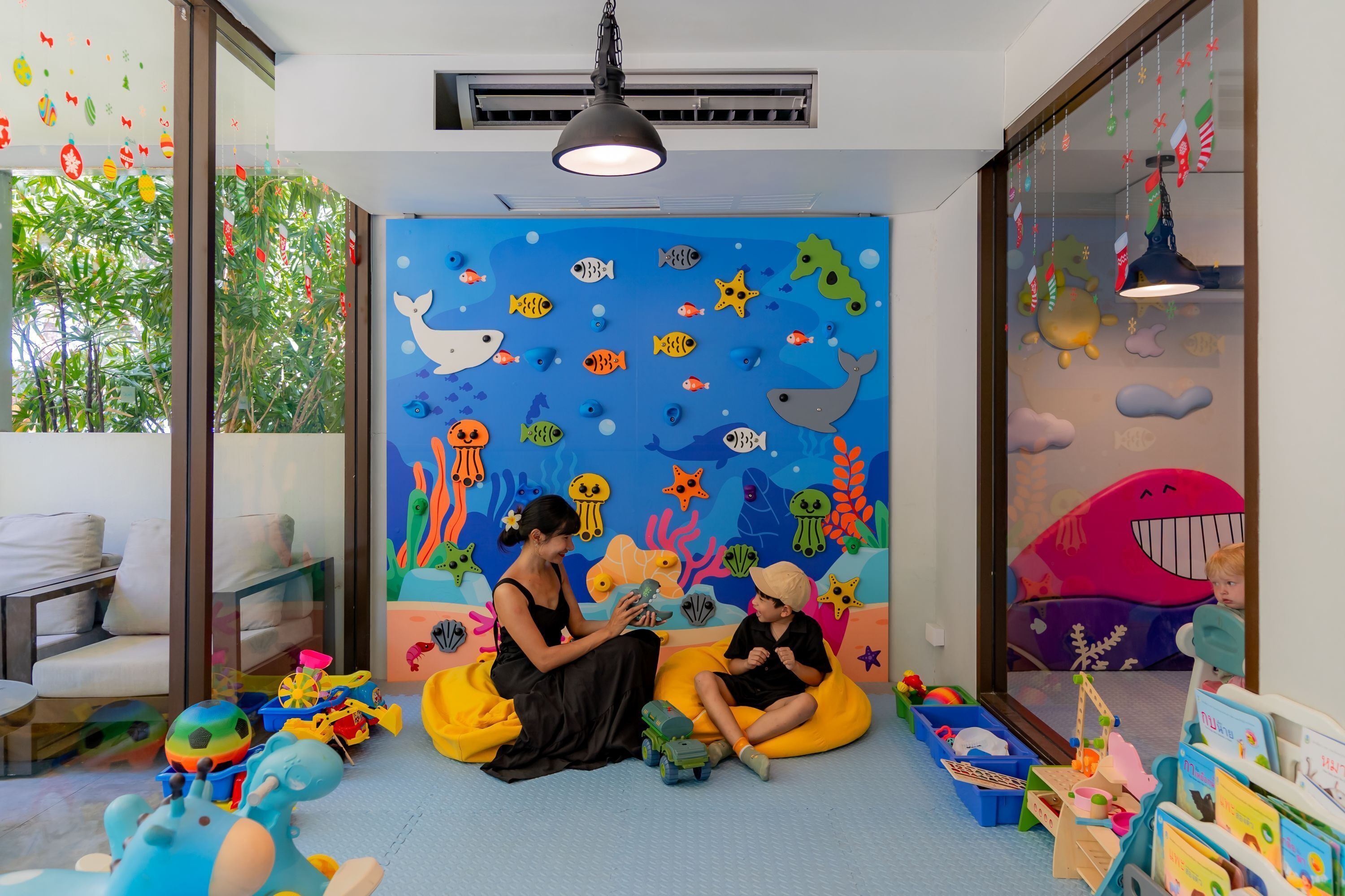 Une pièce avec un mur décoré d’une fresque bleue, un canapé et une fenêtre donnant sur des arbres.