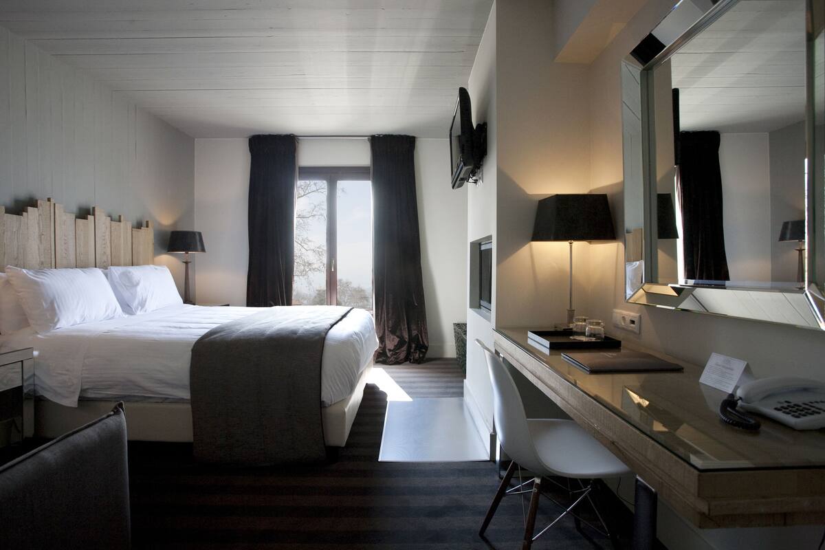 A hotel room with a bed, desk, chair, and a large mirror.