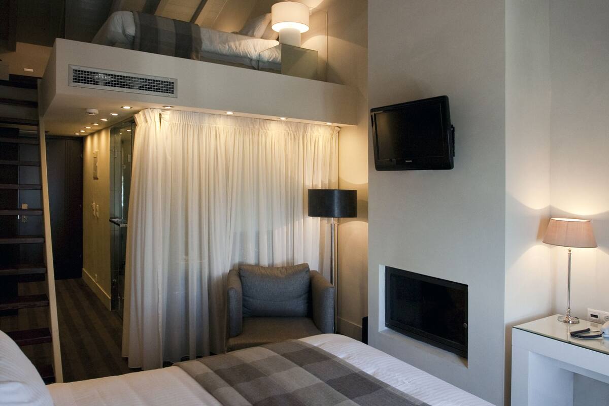 A hotel room with a bed, a television mounted on the wall, and a ceiling with exposed beams.