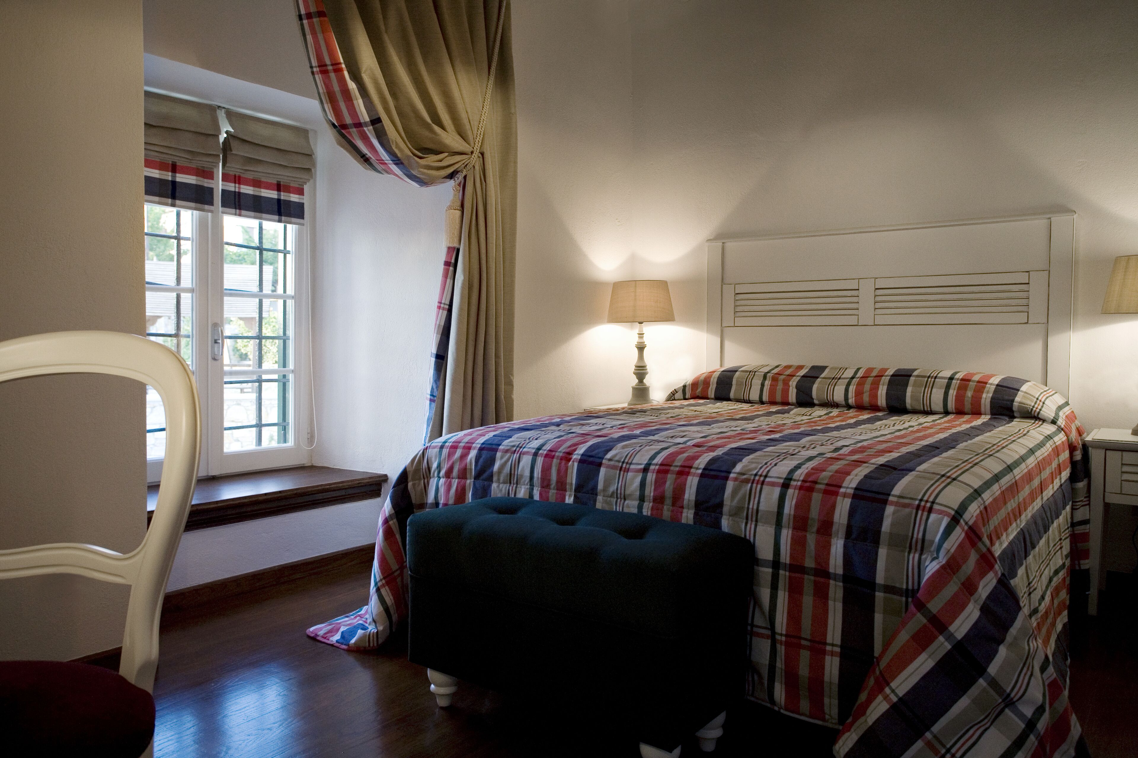 A bedroom with a bed, a chair, a nightstand, a lamp, and a window with curtains.