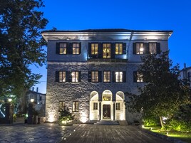 Un edificio de piedra de dos pisos con un porche de madera, múltiples ventanas con contraventanas y una entrada central con arcos.