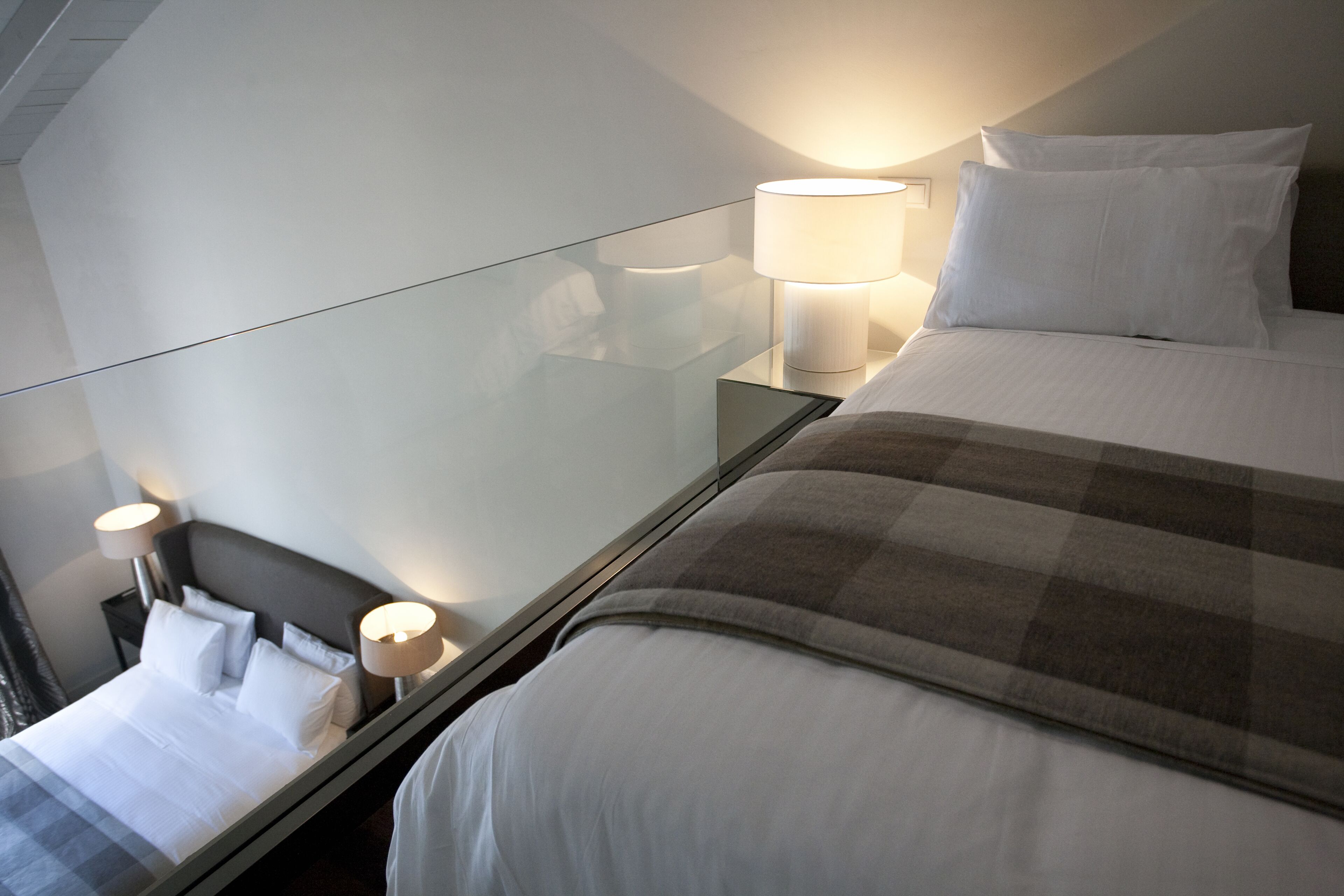 A modern hotel room with a large bed, a glass partition, and two bedside lamps.
