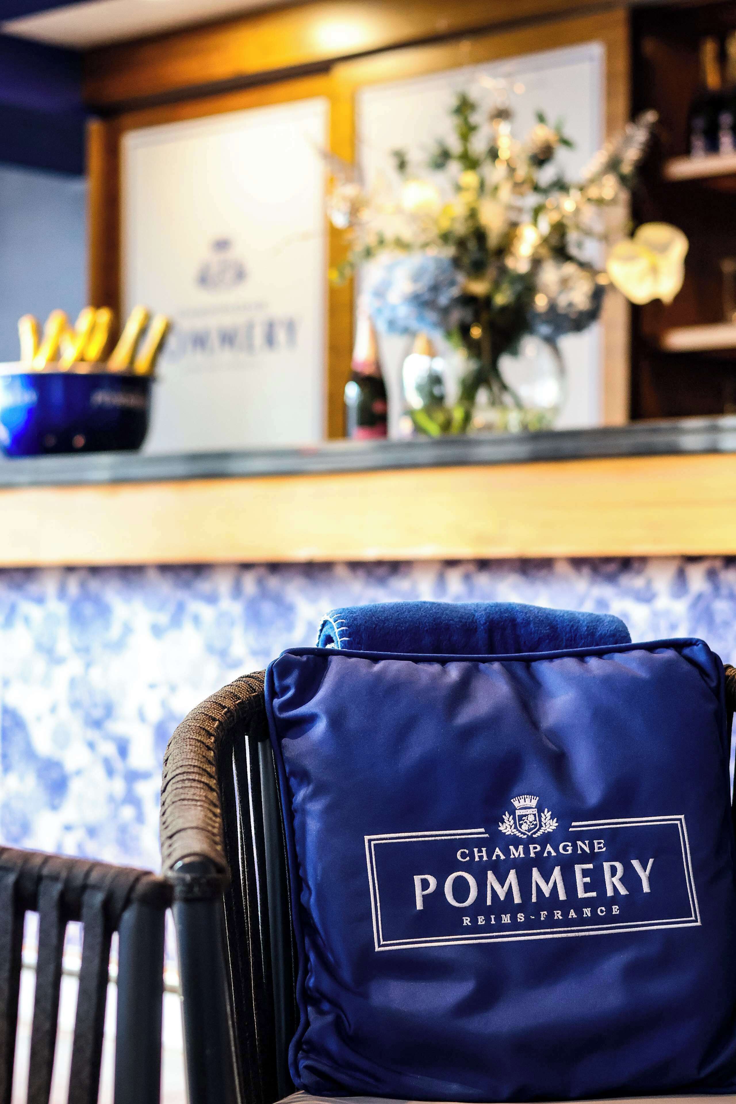 A blue pillow with "Champagne Pommery" branding on a chair.