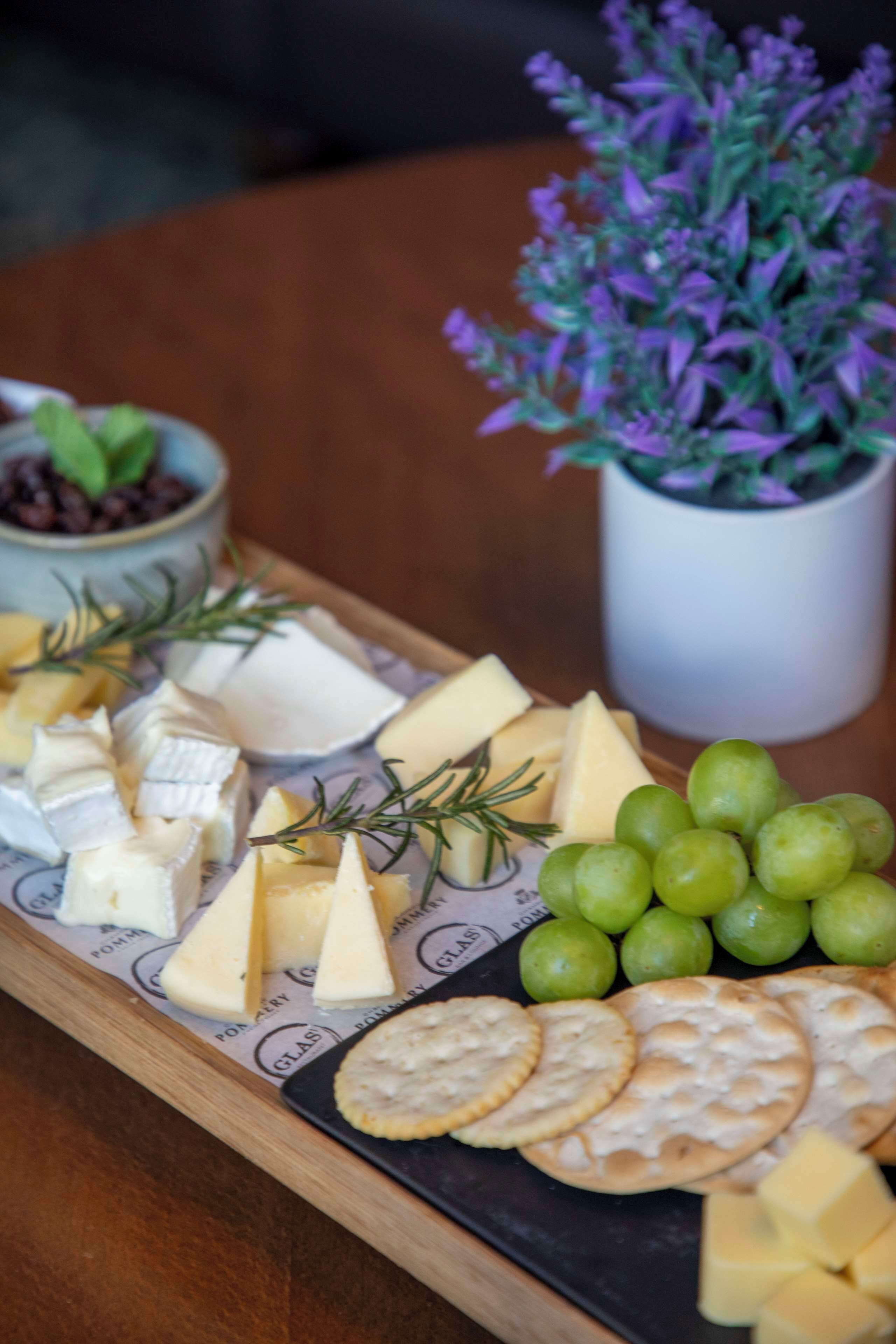 A charcuterie board with various cheeses, crackers, and grapes on a wooden board.