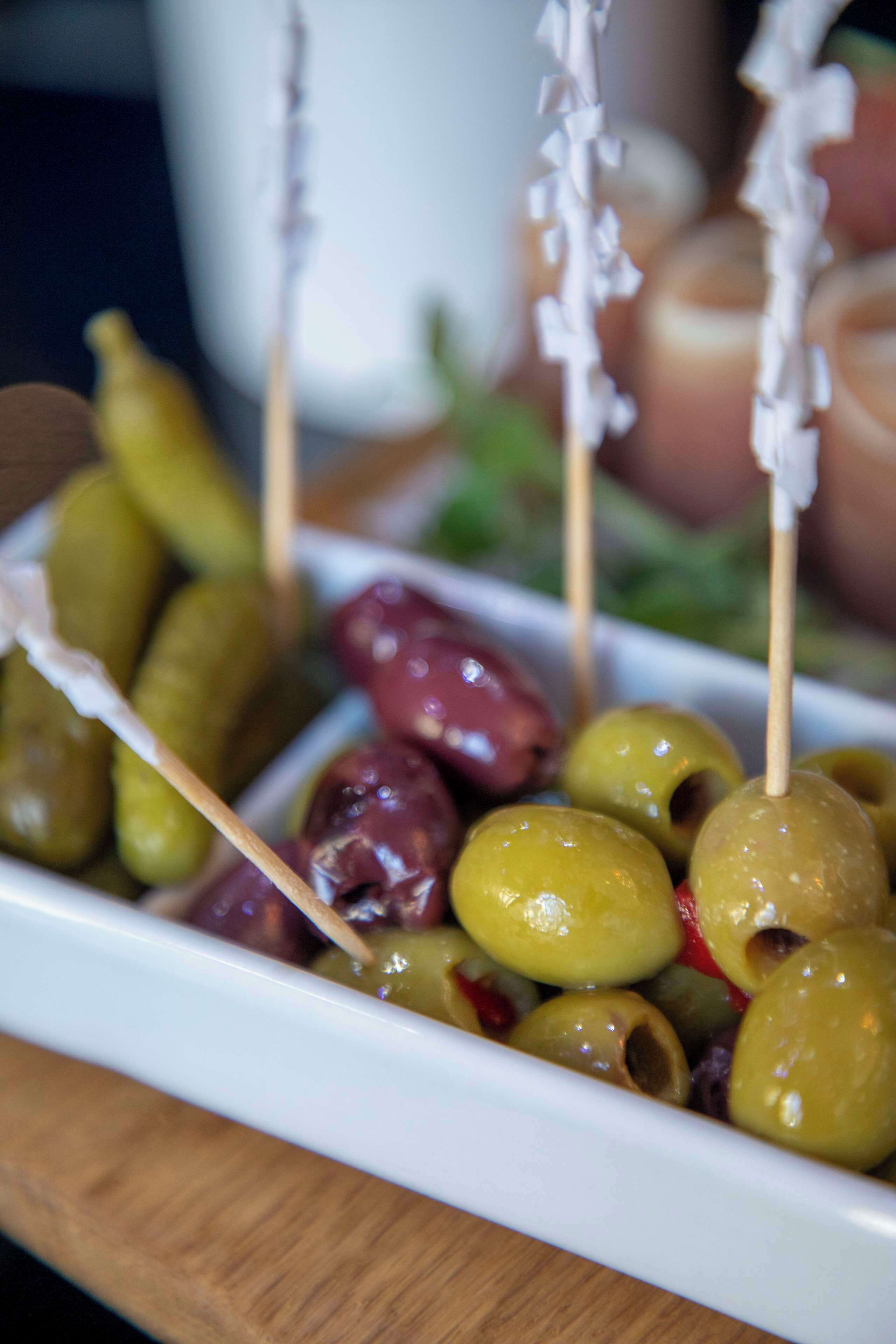 A white plate with olives and cherry tomatoes on skewers.