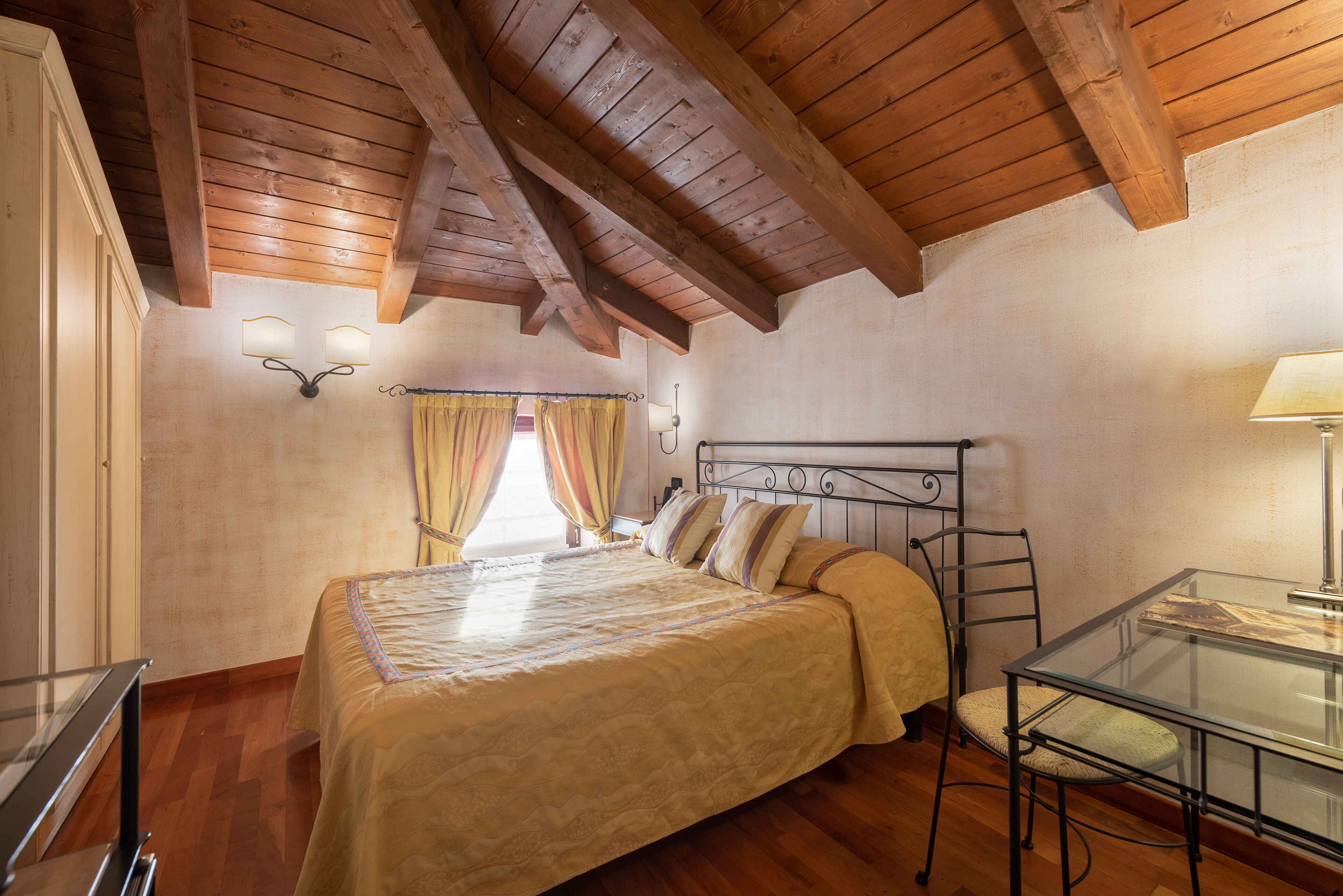 A bedroom with a wooden ceiling, a bed with a headboard, a bedside table, and a chair.