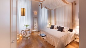 A hotel room with a large bed, a desk with a chair, a small table with a vase, and a hanging light fixture. - Hotel Marco Polo (Verona)