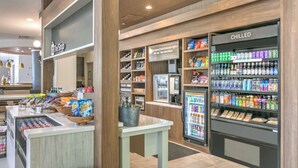 A coffee shop with a refrigerated display, a counter with snacks, and a sign advertising coffee. - Hilton Garden Inn Dallas/Arlington (Arlington)