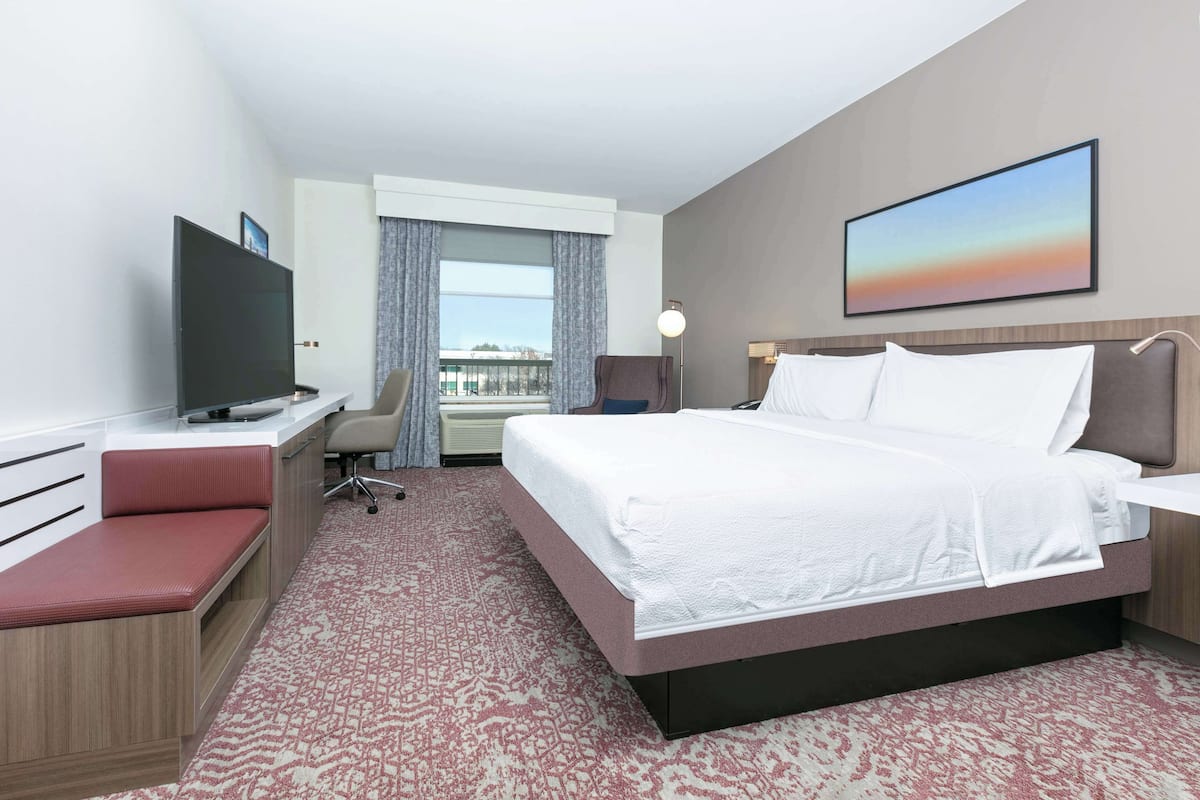 A hotel room with a bed, a desk, a TV, a chair, and a window with curtains.