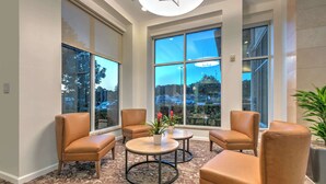 A lobby with leather chairs, a round table, and large windows offering a view of the parking lot and trees. - Hilton Garden Inn Dallas/Arlington (Arlington)