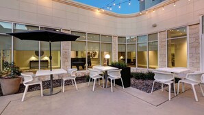 An outdoor patio with white wicker furniture, string lights, and a large umbrella. - Hilton Garden Inn Dallas/Arlington (Arlington)