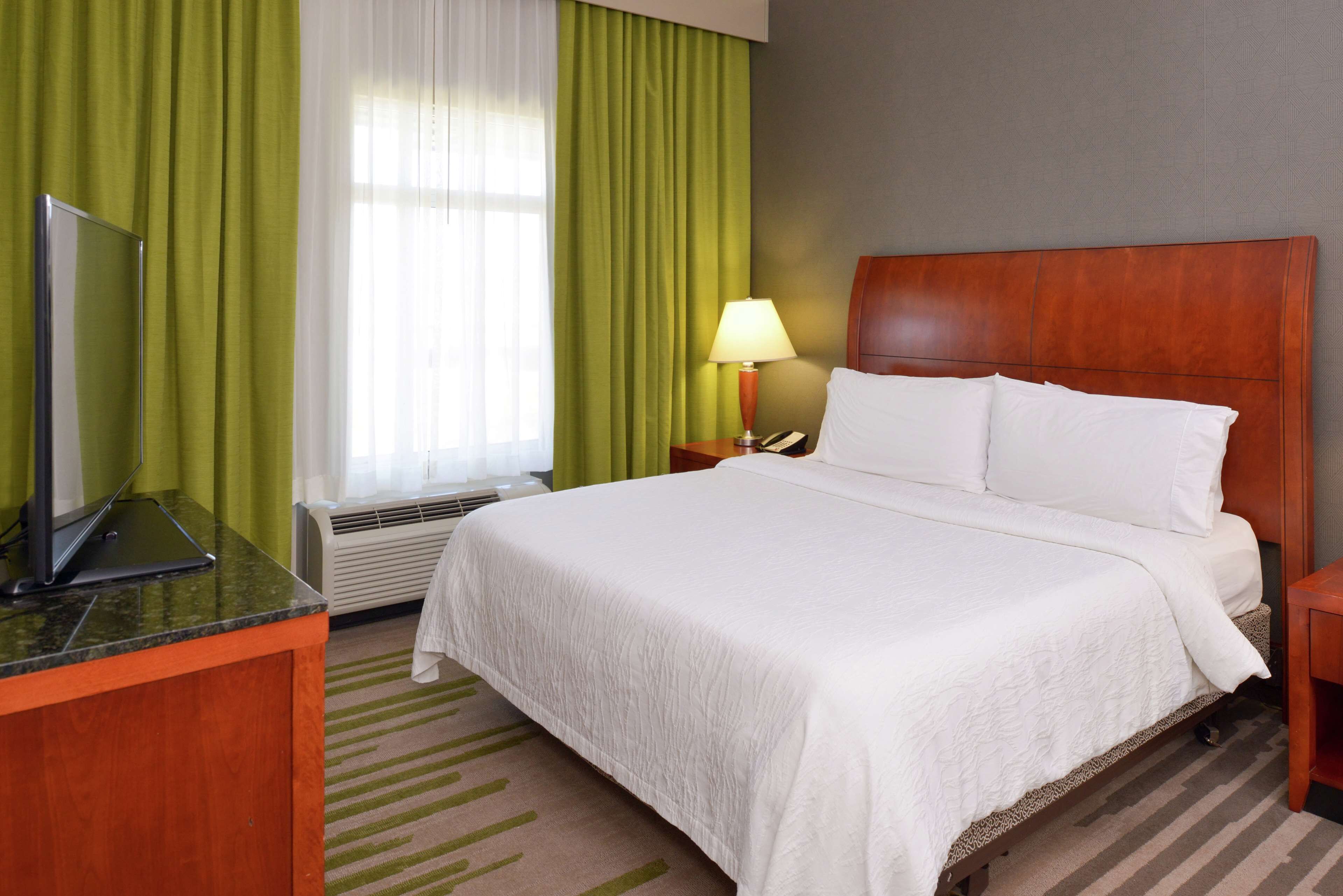 A hotel room with a bed, a desk with a laptop, a lamp, and a window with curtains.