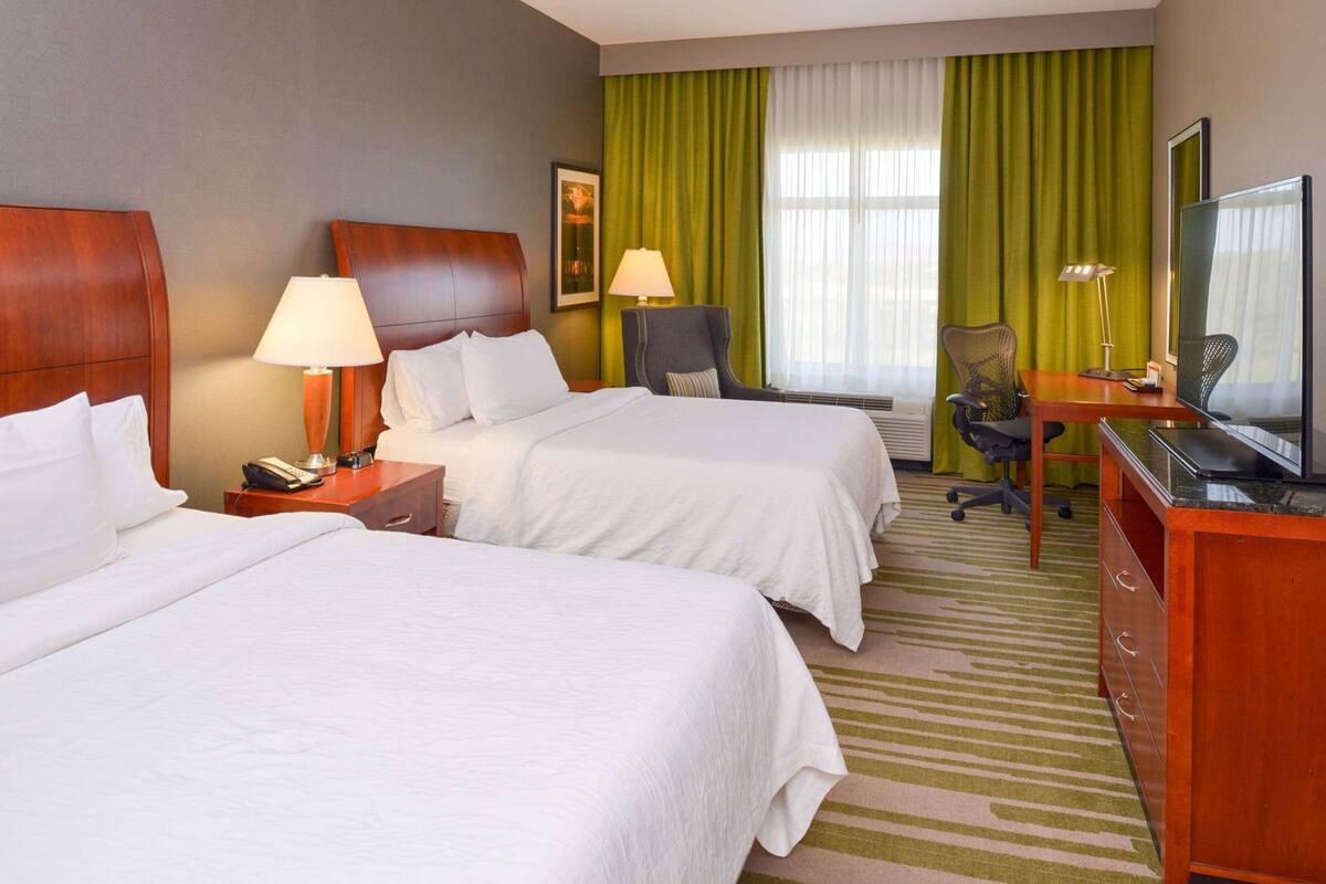 Une chambre d’hôtel avec deux lits, un bureau avec un ordinateur, une chaise, une télévision et une lampe.