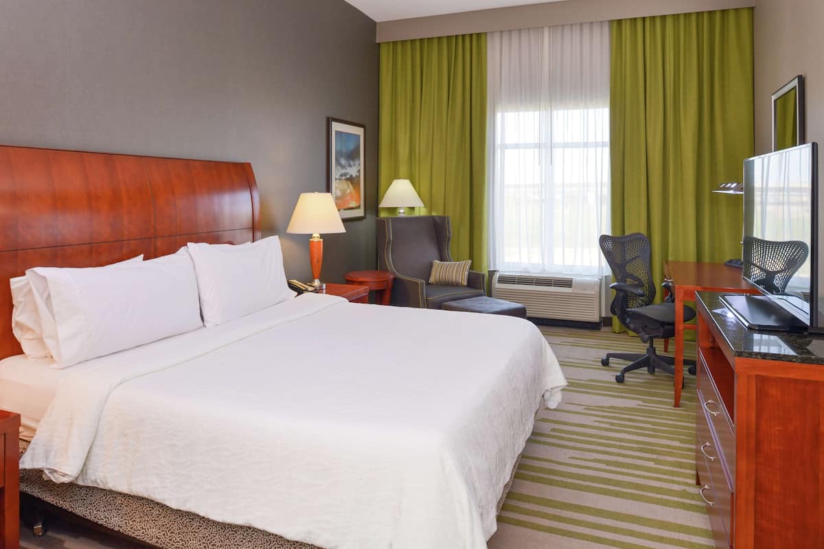 Une chambre d’hôtel avec un grand lit, deux tables de chevet, un bureau avec une chaise, une télévision et une fenêtre avec des rideaux.
