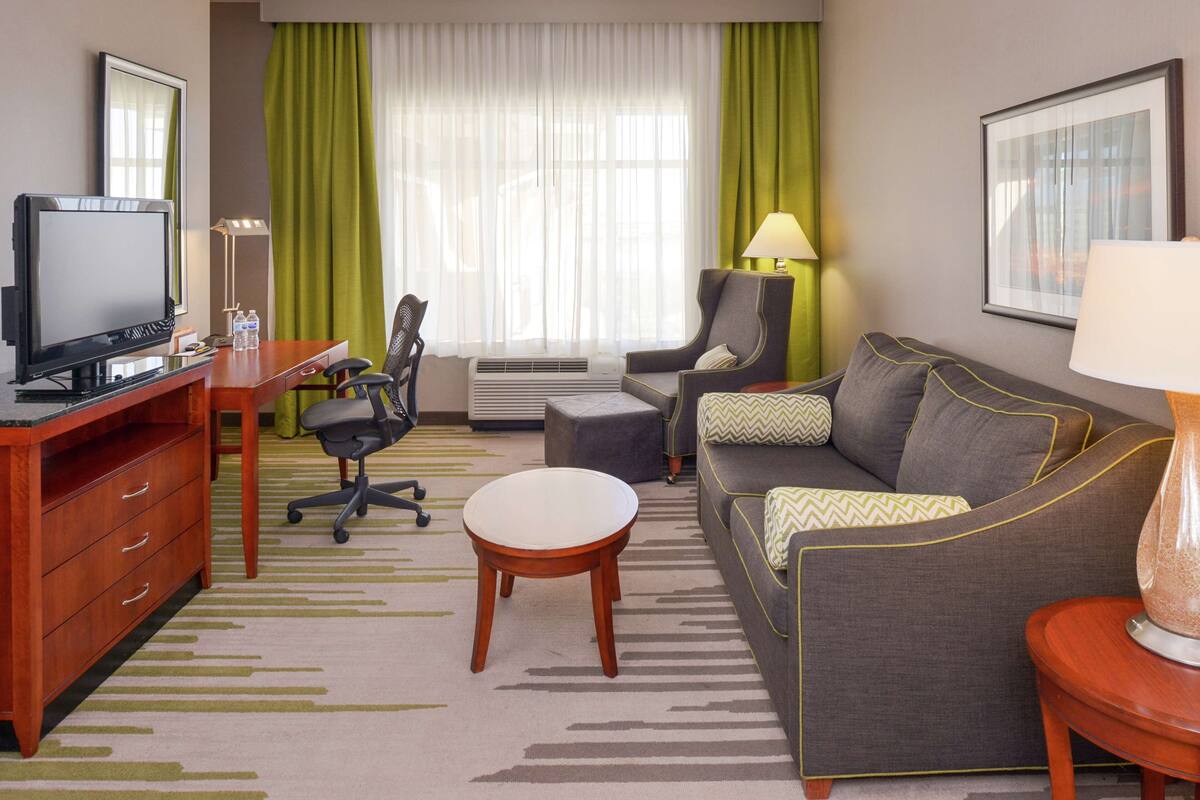 Une chambre d’hôtel équipée d’une télévision, d’un bureau, d’une chaise, d’un canapé et d’une petite table ronde.
