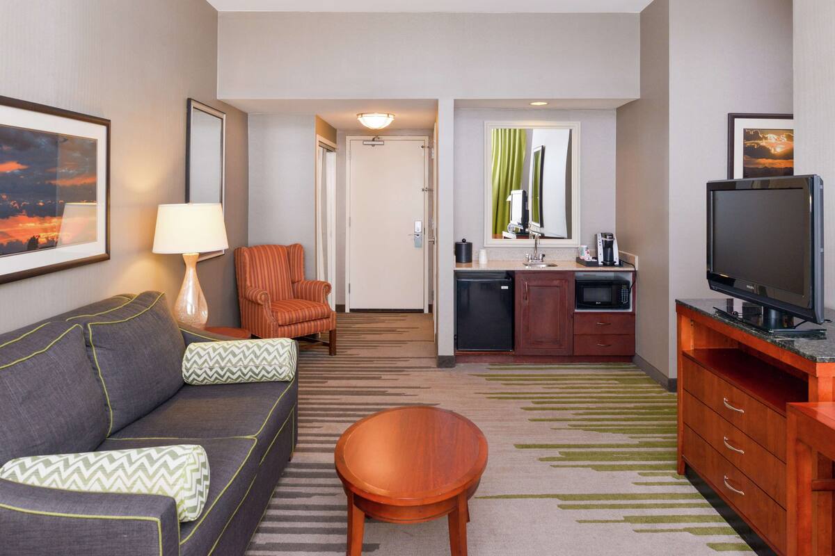 Une chambre d’hôtel équipée d’un canapé, d’une table basse en bois, d’une télévision, d’une kitchenette et d’une porte donnant sur une autre pièce.