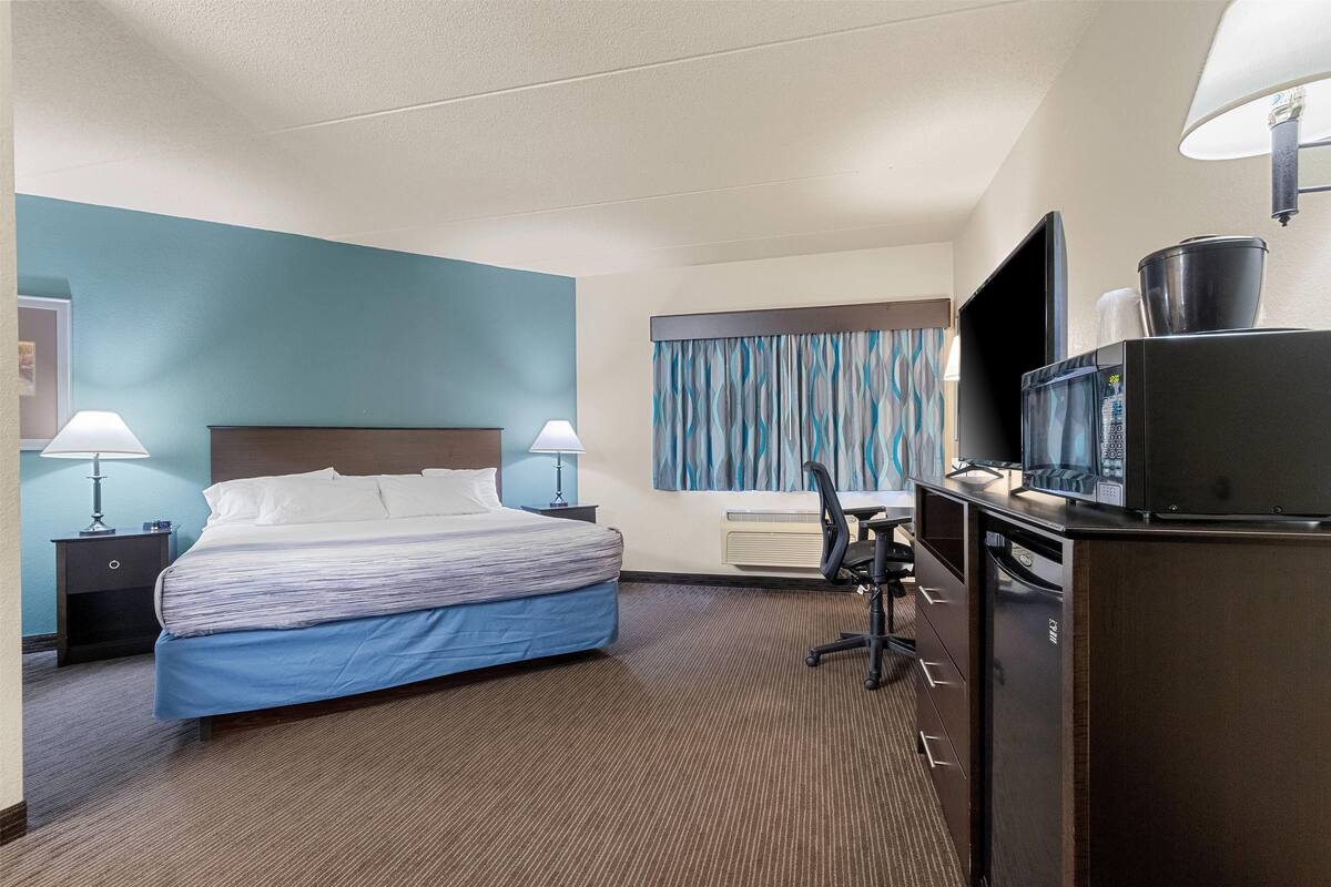 Ein Hotelzimmer mit Bett, Schreibtisch, Stuhl, Fernseher und Mikrowelle.