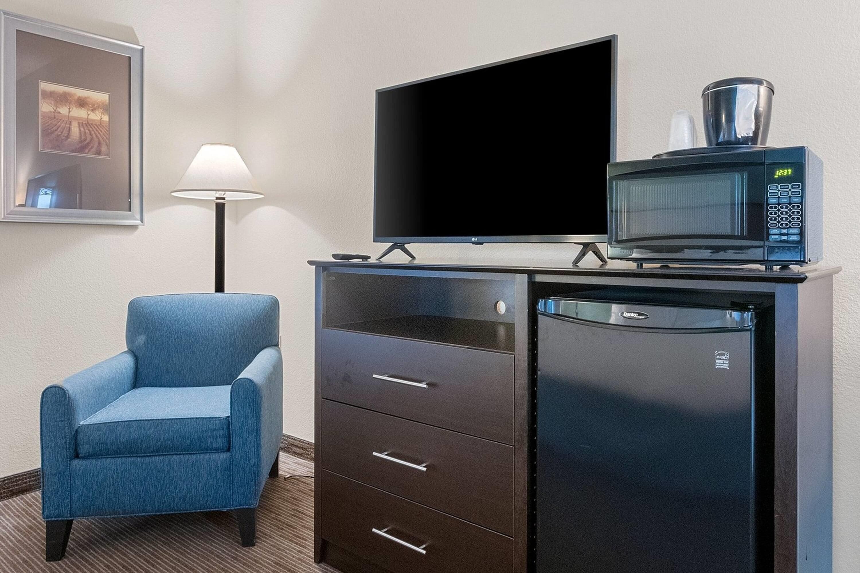 A hotel room with a flat-screen TV, a microwave, a blue armchair, and a cabinet with drawers.