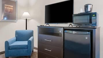 Habitación de hotel con televisión de pantalla plana, microondas, un sillón azul y un mueble con cajones.
